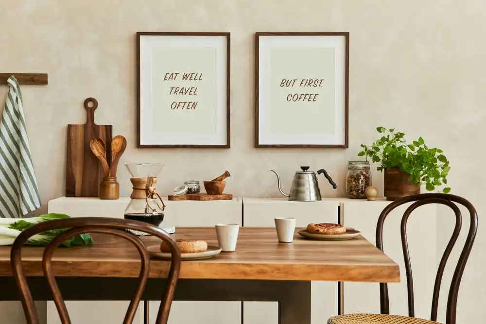 Jídelní stůl z masivního dřeva s kovovým podstavcem. U stolu jsou dvě dřevěné židle. Na stole jsou položené dva talíře s pečivem a dva hrnky kávy. Na stole je také karafa s kávou.