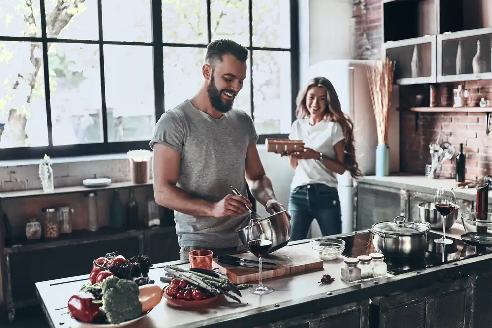 Muž a žena připravují jídlo v moderní kuchyni, muž míchá ingredience v misce a žena se směje.
