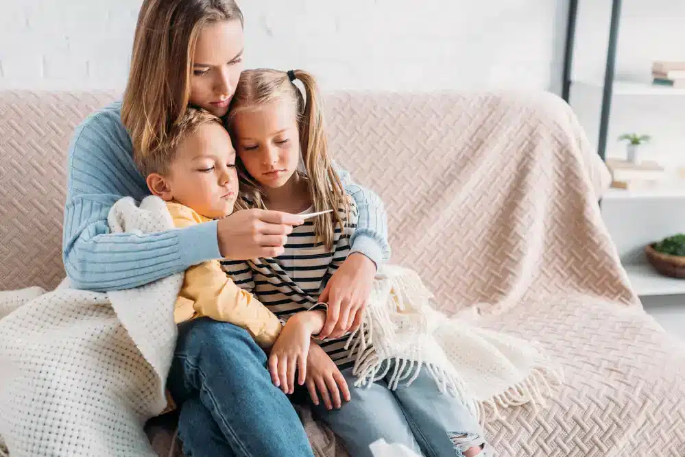 Matka s dcerou a se synem na gauči koukající se na tělesný teploměr.