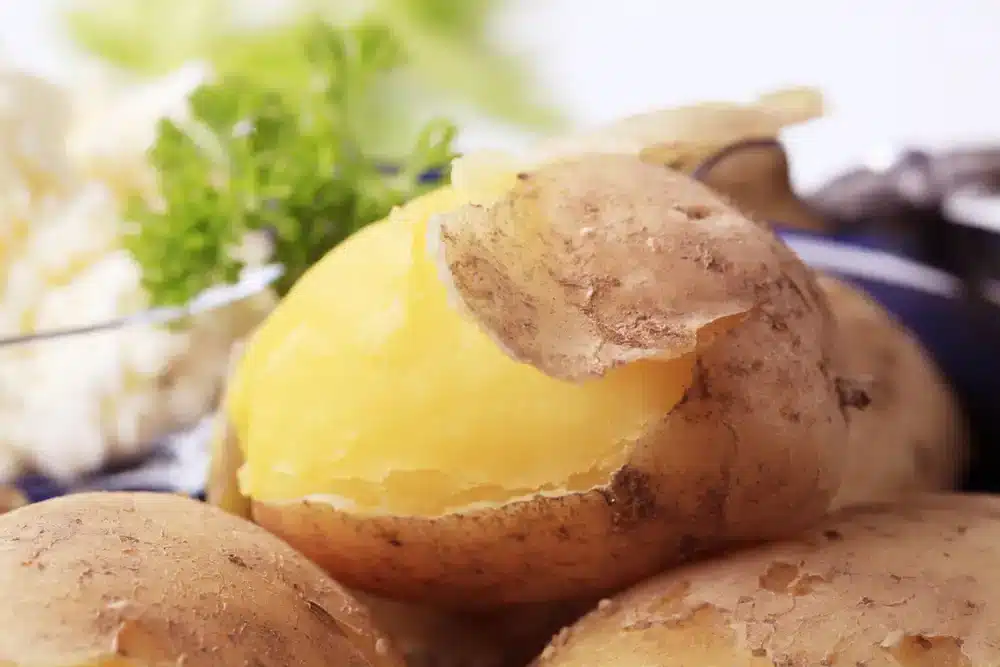 Uvařené brambory ve slupce na talíři, připravené k oloupání a podávání jako příloha nebo k další úpravě.