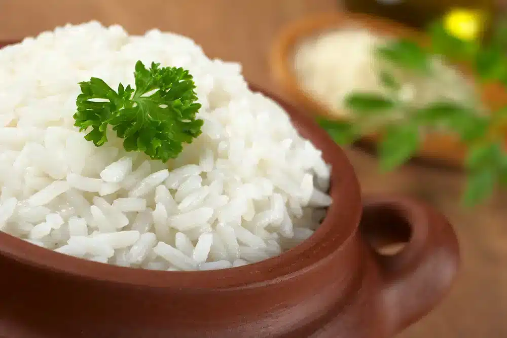Hrnec s chutnou nadýchanou bílou rýží ozdobenou petrželkou na tmavém podkladu.