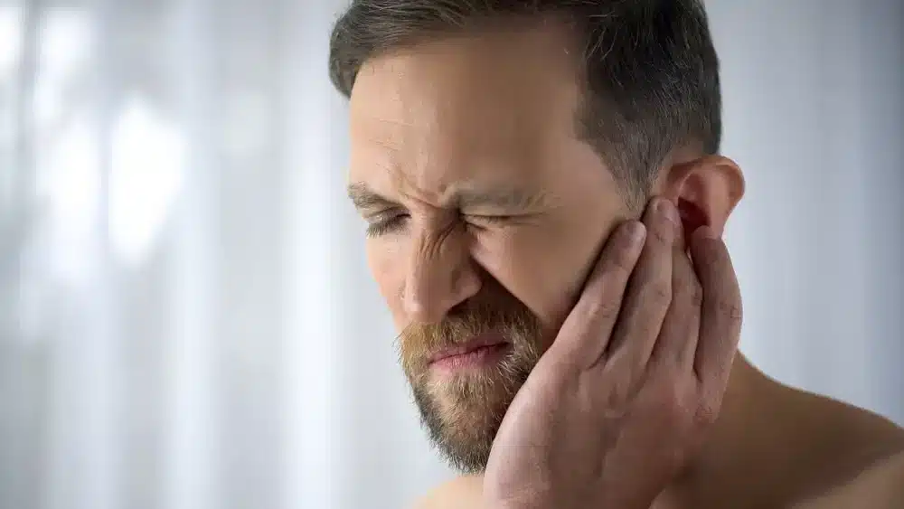 Muž si masíruje oblast ucha a čelisti, což je technika, která může zmírnit nepohodlí způsobené tinnitem a napomoci cirkulaci v této oblasti.
