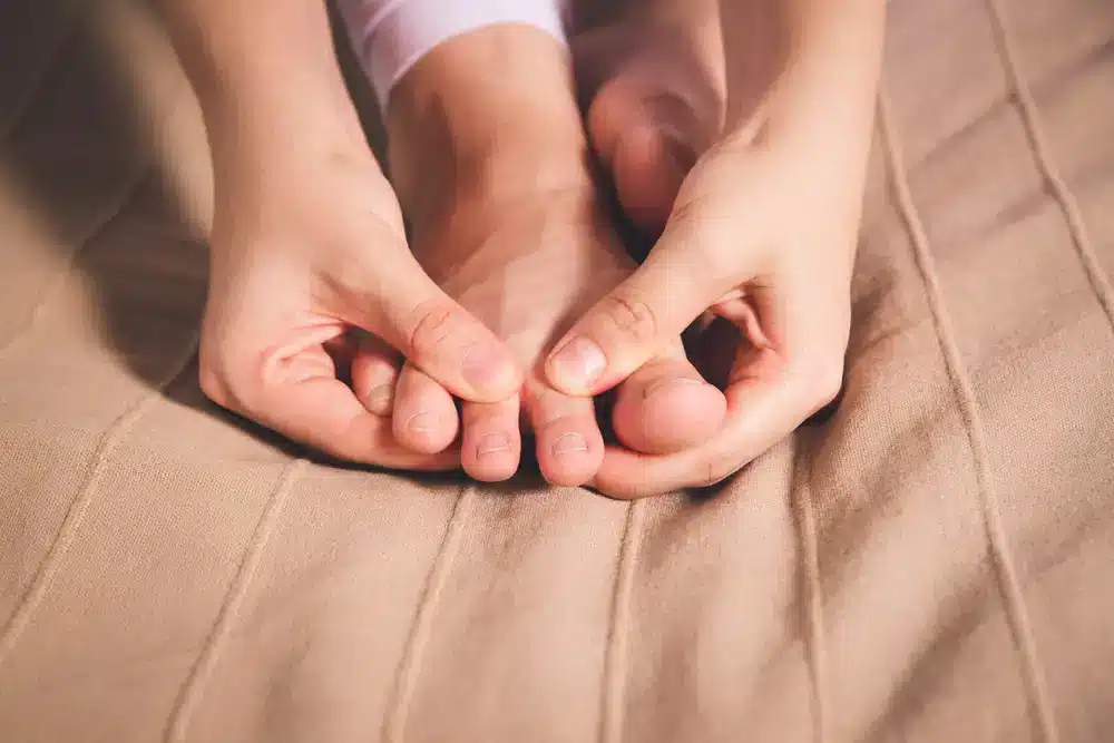 Osoba si prohmatává oblast kolem palce na noze, což může být spojeno s léčbou dnavých symptomů.