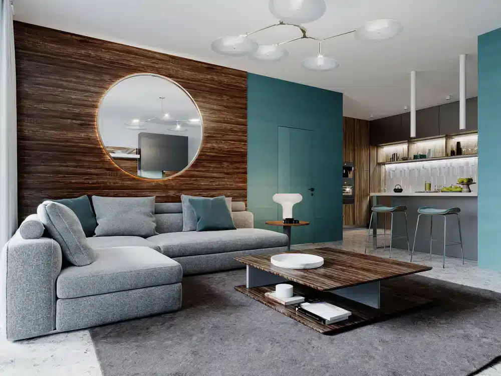 Elegantní obývací pokoj s modrozelenými stěnami a dřevěným obložením. Velké kruhové zrcadlo nad pohovkou.
