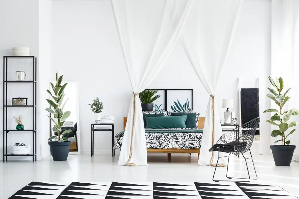 Obrázek zobrazuje obývací pokoj s černobílým motivem a kontrastními textilními vzory. Otevřené prostory a vysoké stropy jsou využity s vysokými rostlinami a štíhlým nábytkem, což přináší do malého bytu vzdušnost a styl.