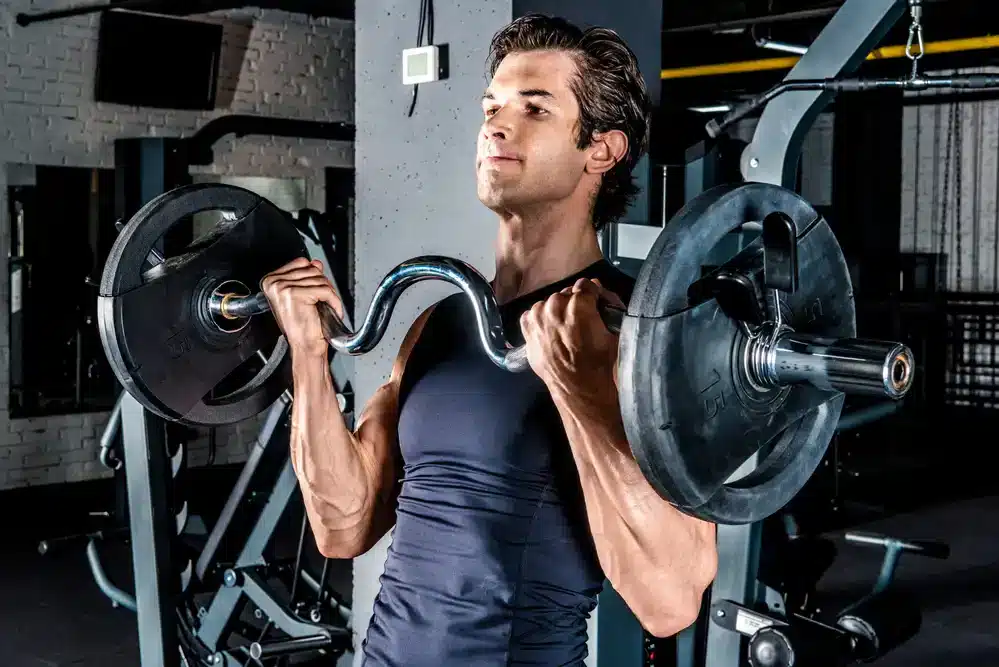 Muž provádějící bicepsový zdvih s činkou v posilovně, ukazující důležitost fyzického cvičení pro zvýšení testosteronu.