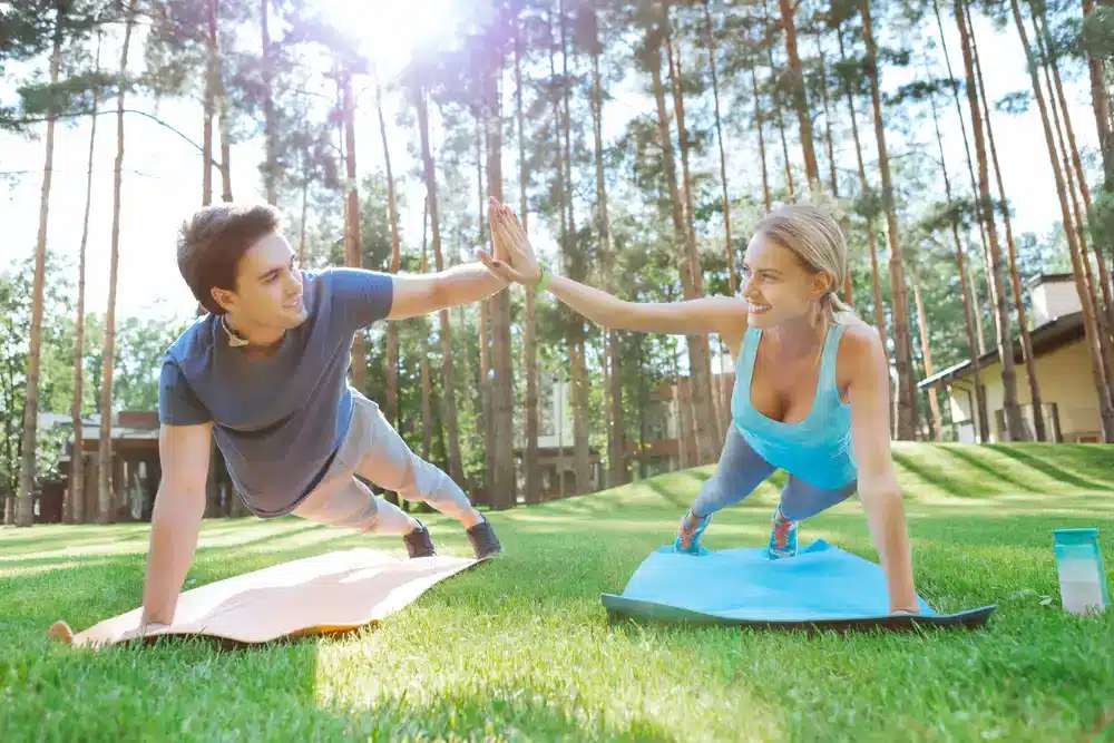 Dvojice dělá plank na jóga podložkách venku, ukázka vysoko intenzivního intervalového tréninku pro zvýšení metabolické rychlosti.