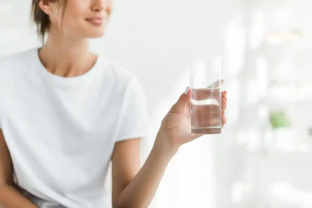 Žena drží sklenici vody, což připomíná, že pití studené vody může urychlit metabolismus.