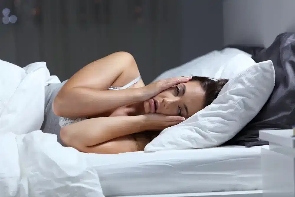 Žena ležící v posteli a neschopná usnout kvůli psychickému napětí a příznakům vyhoření.